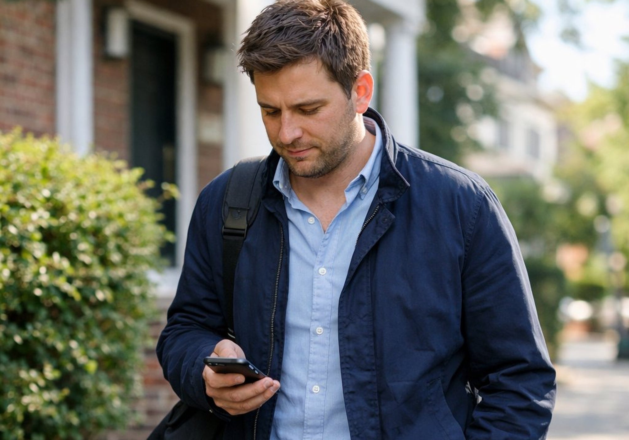 Man in a blue jacket and light blue shirt using a phone outdoors.